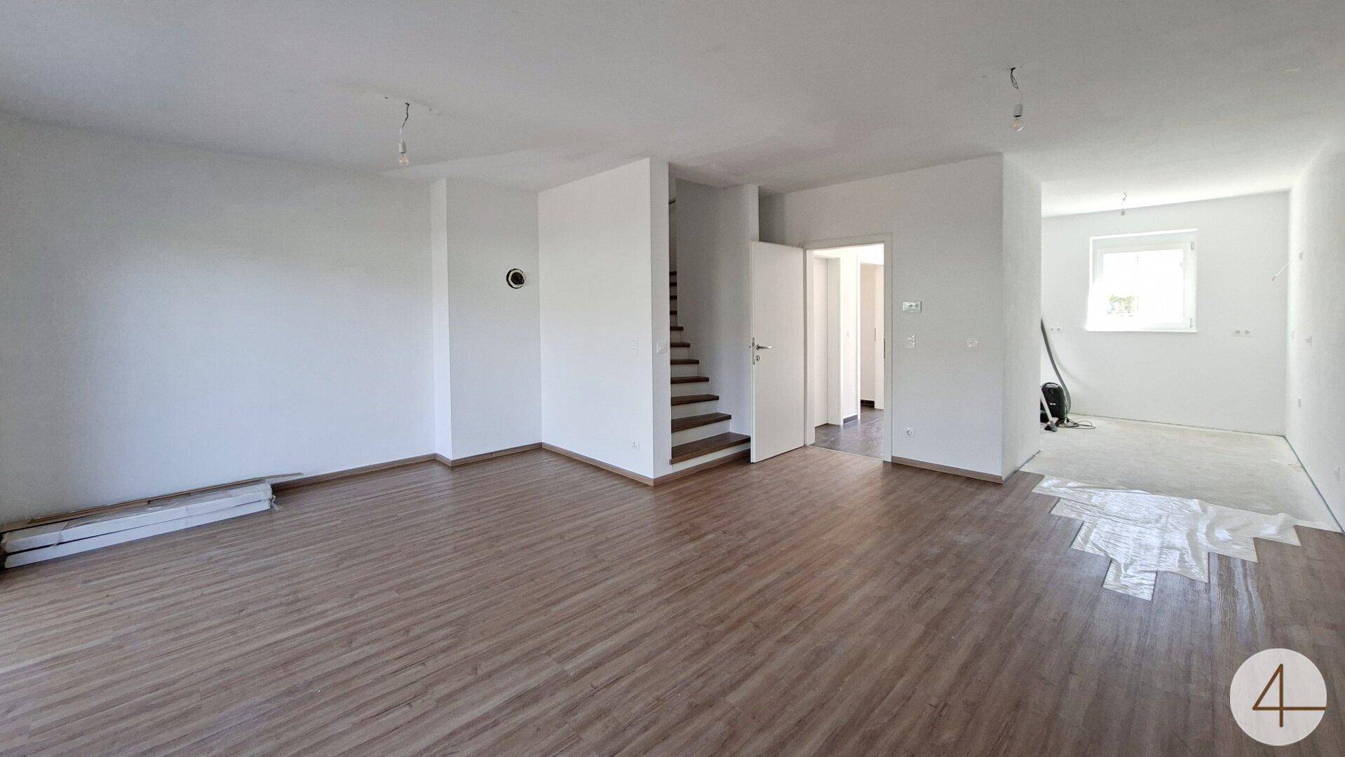 Geräumiges Wohnzimmer mit hellem Laminatboden und Zugang zu weiteren Räumen.