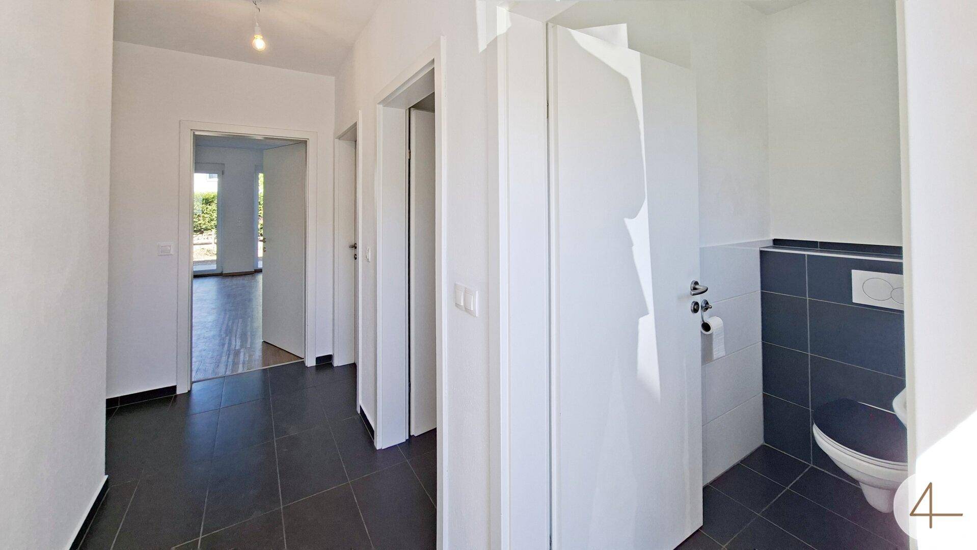 Heller Flur mit dunklen Fliesen und angrenzendem Gäste-WC mit Wand-WC.