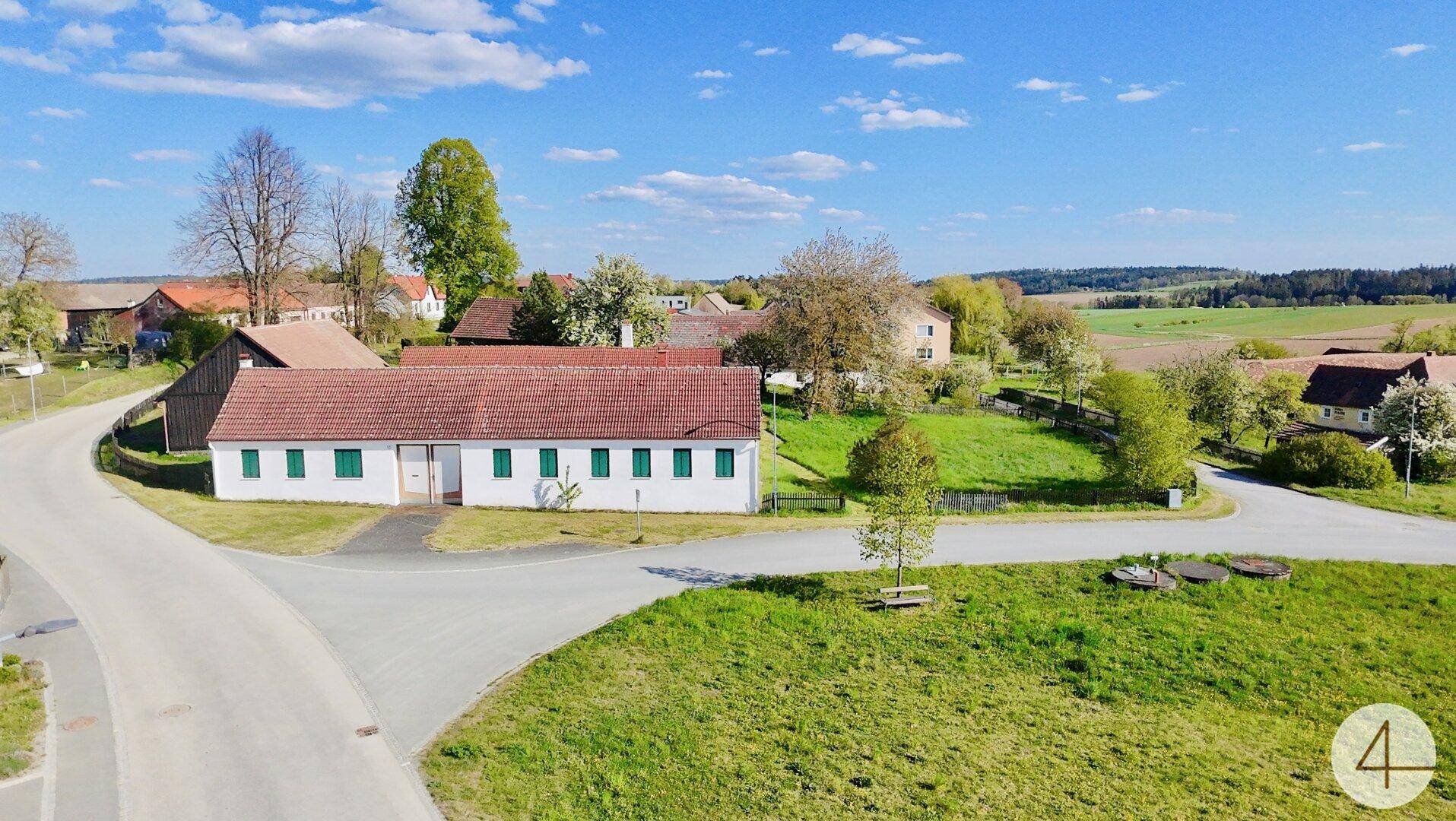 Idyllisches Anwesen in ländlicher Umgebung mit weiß getünchten Gebäuden und roten Ziegeldächern unter blauem Himmel.