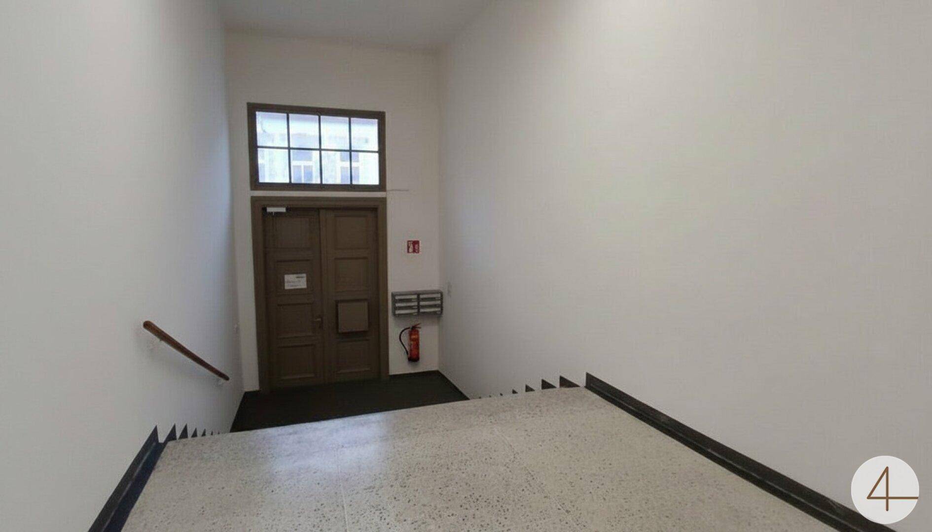 Treppenhaus mit Terrazzoboden und Eingangstür, die zu den oberen Etagen führt.