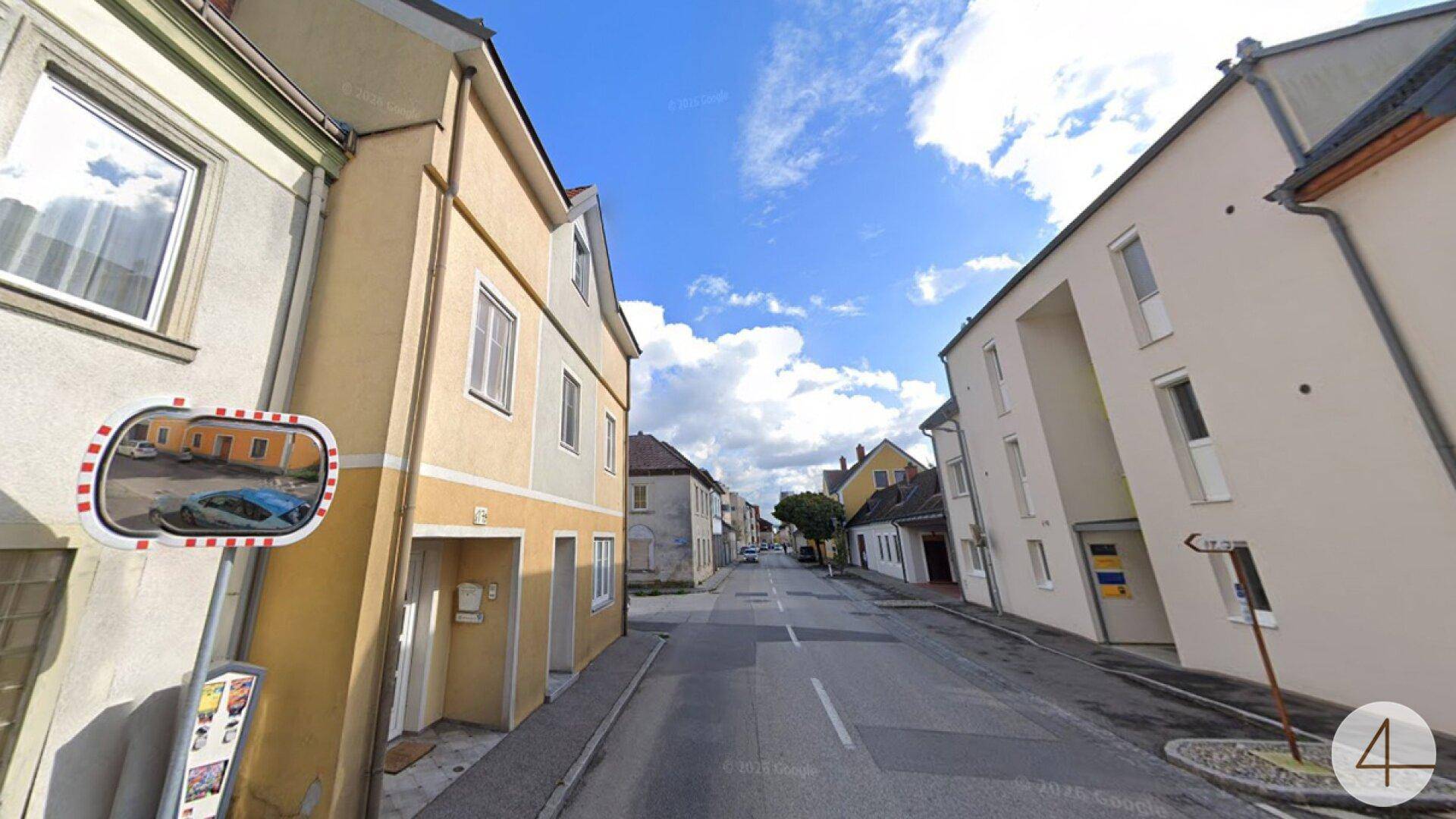 Perspektive einer Wohnstraße mit dem gelben Gebäude auf der linken Seite und einem Verkehrsspiegel.