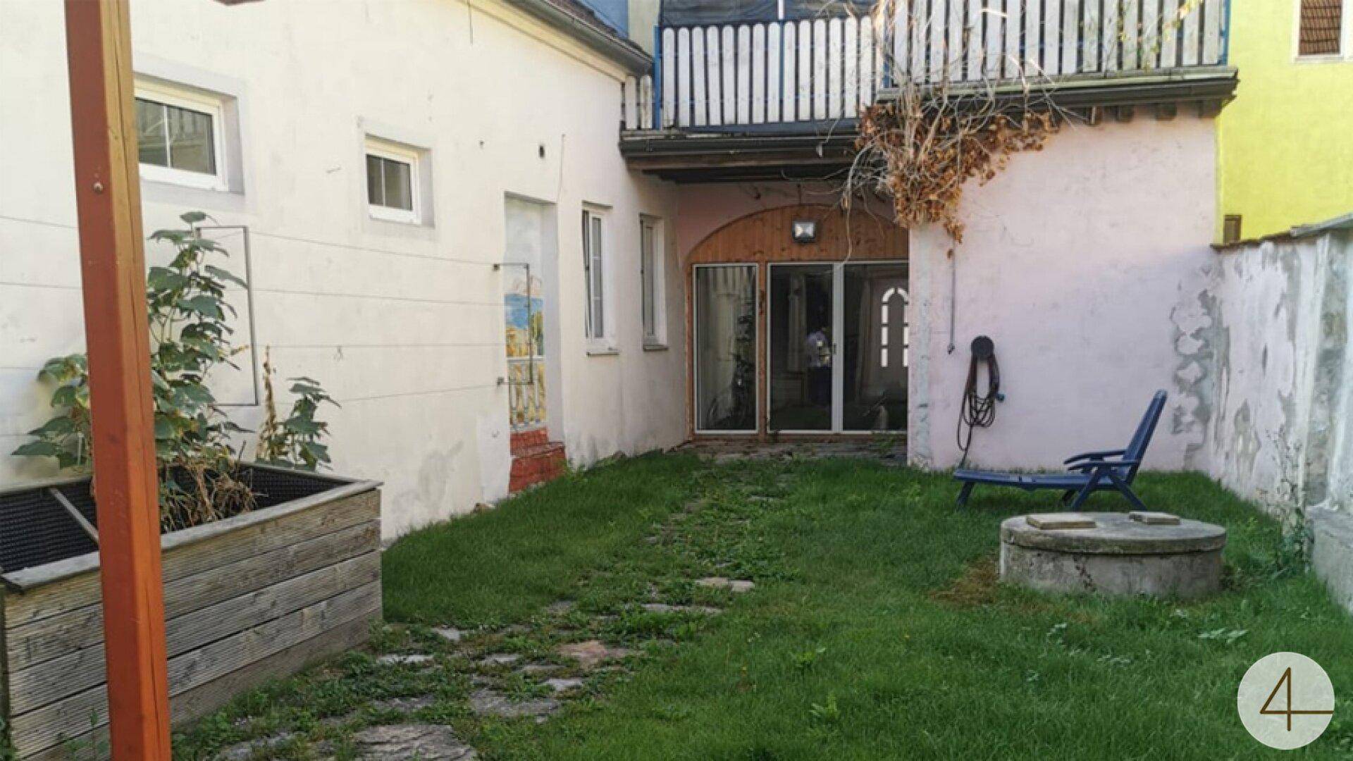 Kleiner Hinterhofgarten mit Rasenfläche, Holzpflanzkasten und einem Balkon im oberen Bereich.