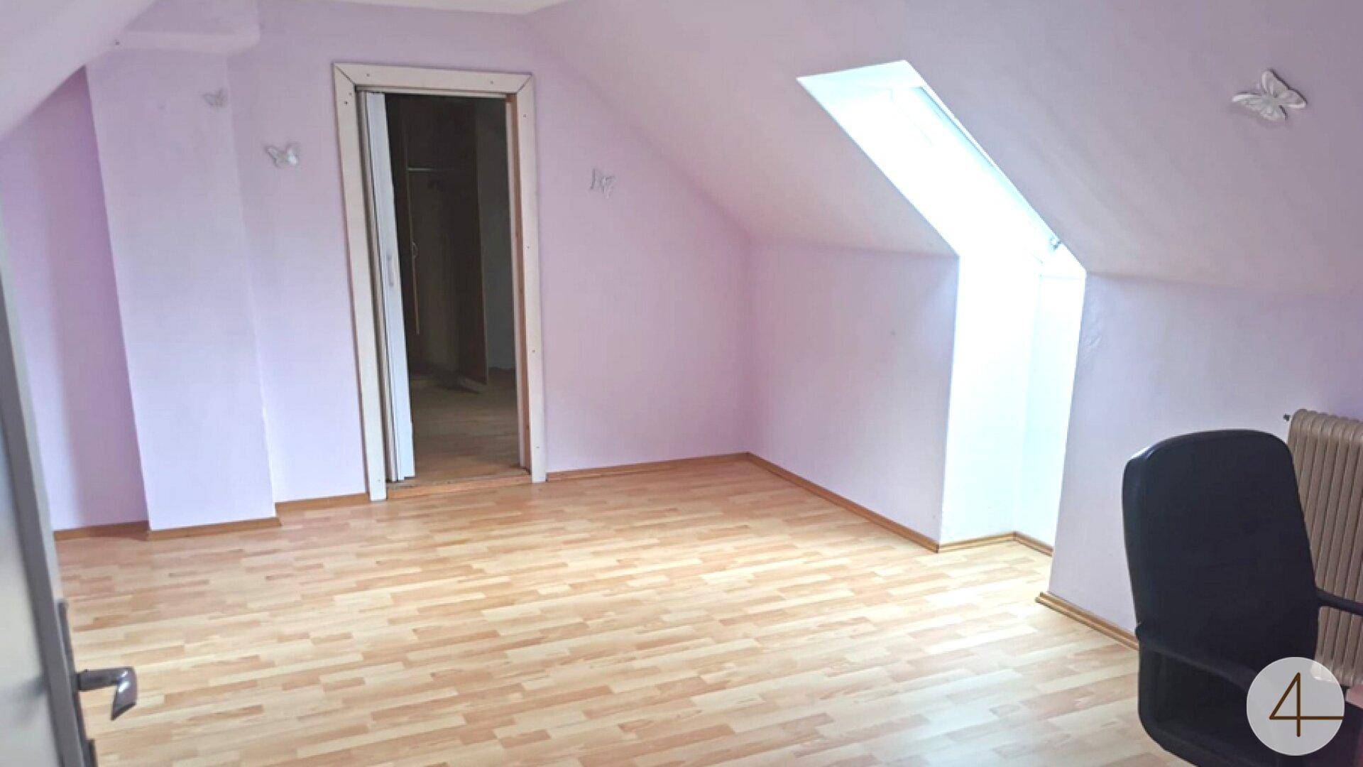Dachzimmer mit schrägen Wänden, lila Anstrich, Laminatboden und einem großen Dachfenster.