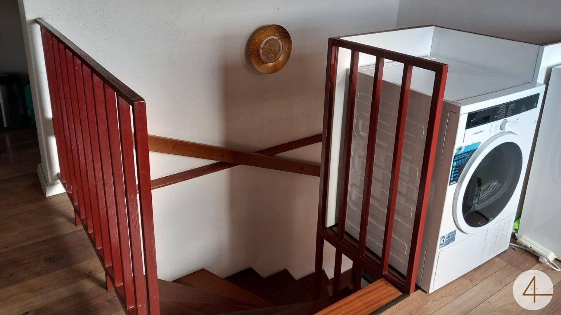 Praktischer Bereich mit Waschmaschine und Holztreppe, ideal für den täglichen Gebrauch.