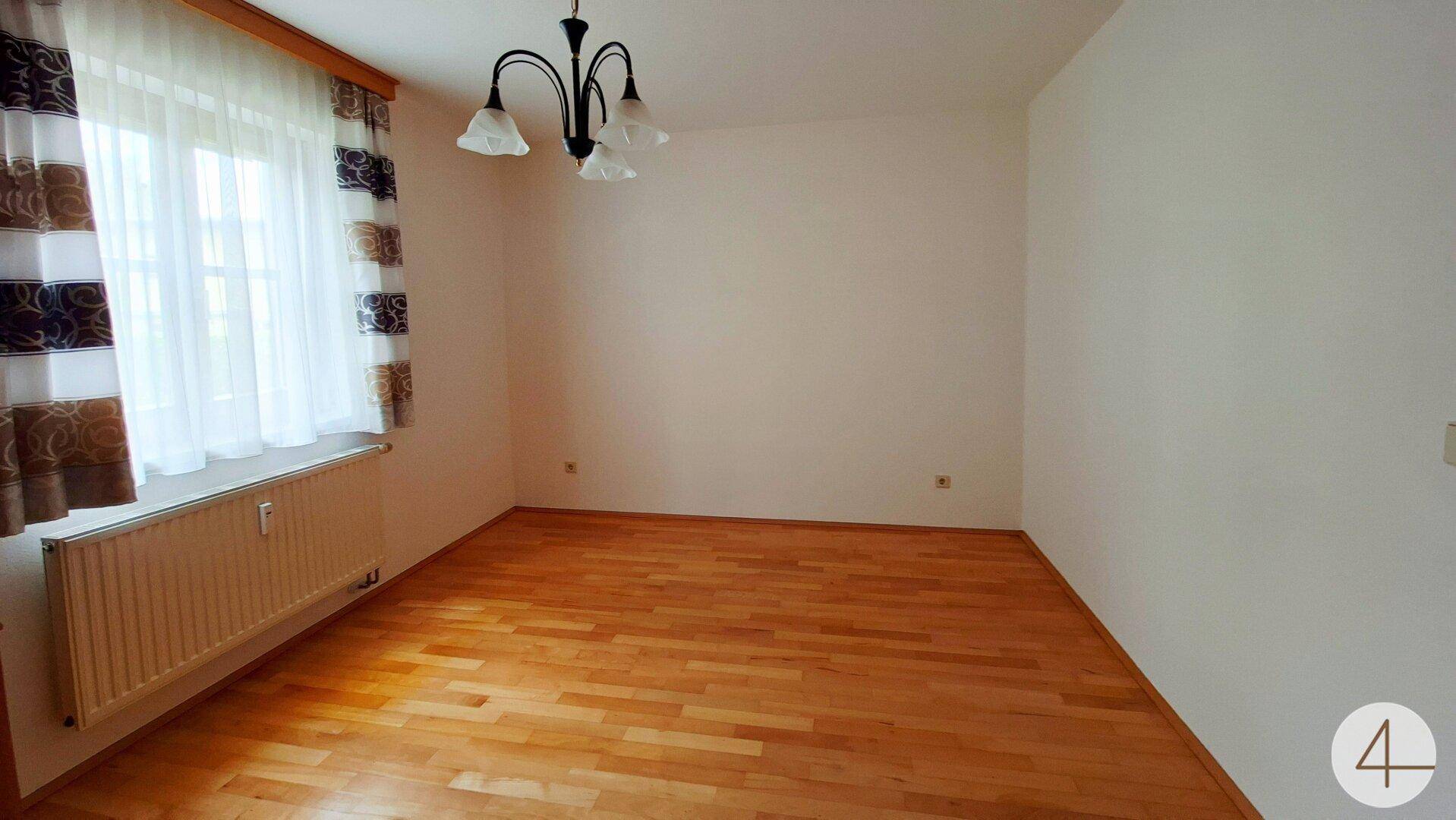 Leeres Zimmer mit Holzparkettboden, großem Fenster und Heizkörper.