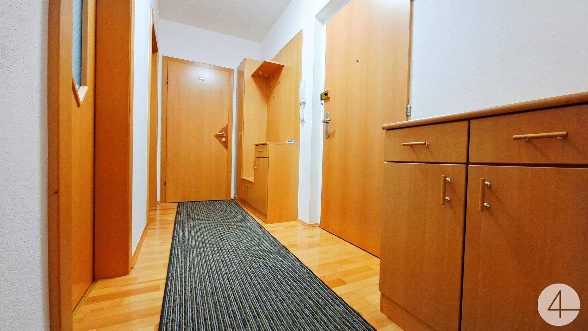Heller Flur mit Holzparkettboden, Garderobe und Eingangstür.