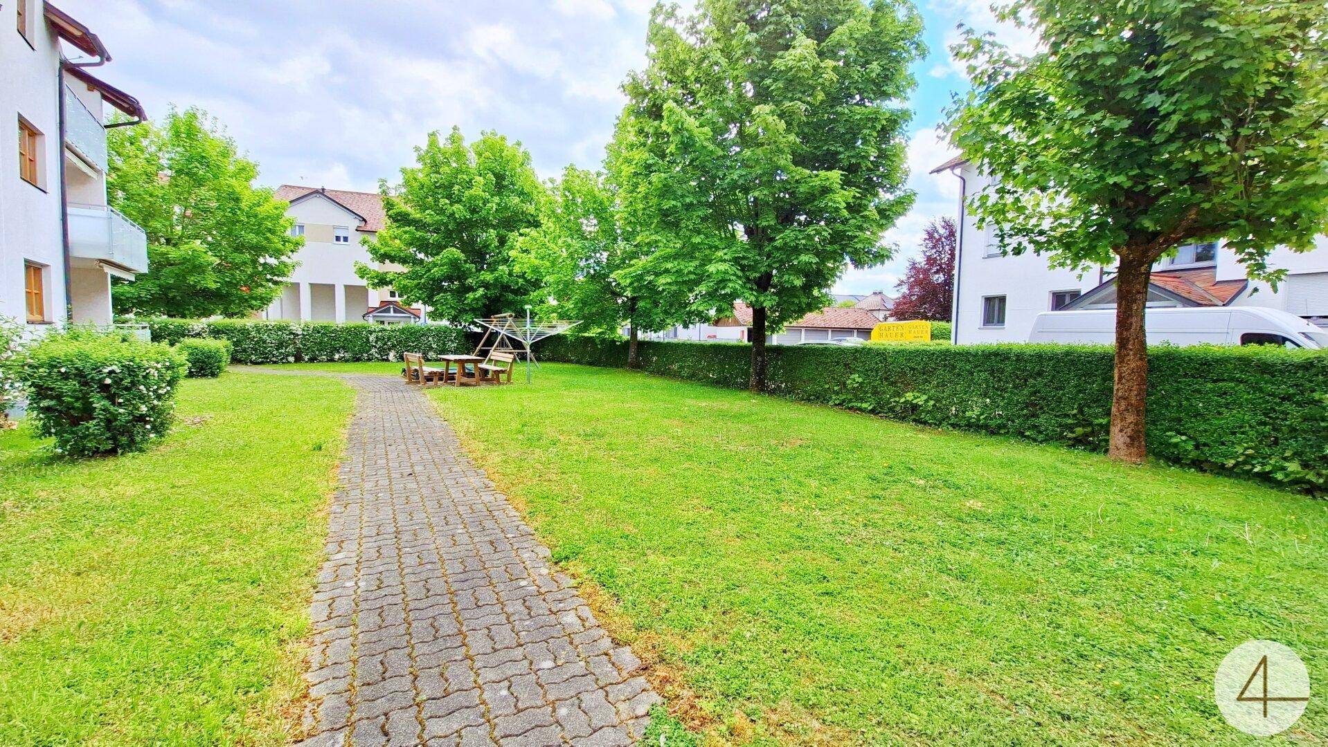 Gemeinschaftlicher Gartenbereich mit Rasenfläche, Bäumen und Sitzgelegenheit.