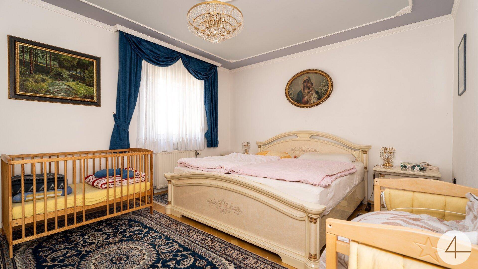 Helles Schlafzimmer mit klassischem Doppelbett, Kinderbett und einem gemusterten Teppich.