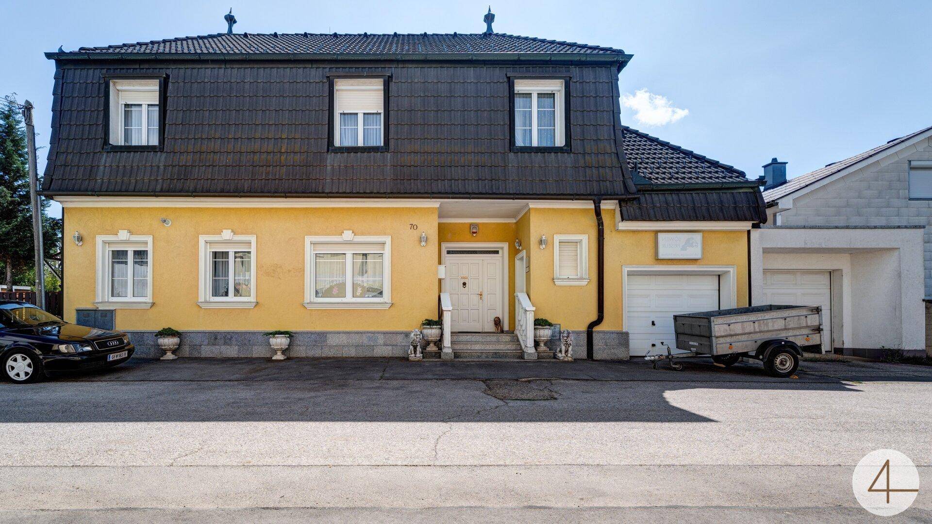 Frontansicht des gelben Hauptgebäudes mit Mansarddach, weißen Fenstern und einer Garage.