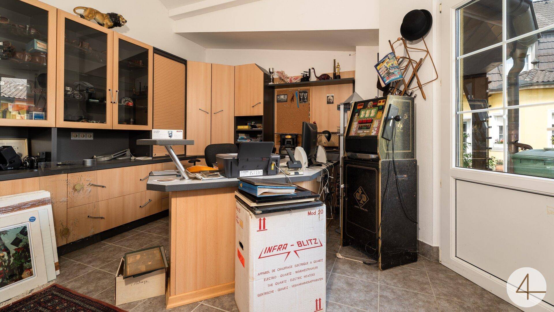 Büroähnlicher Raum mit Holzschränken, Schreibtisch und einem Spielautomaten.