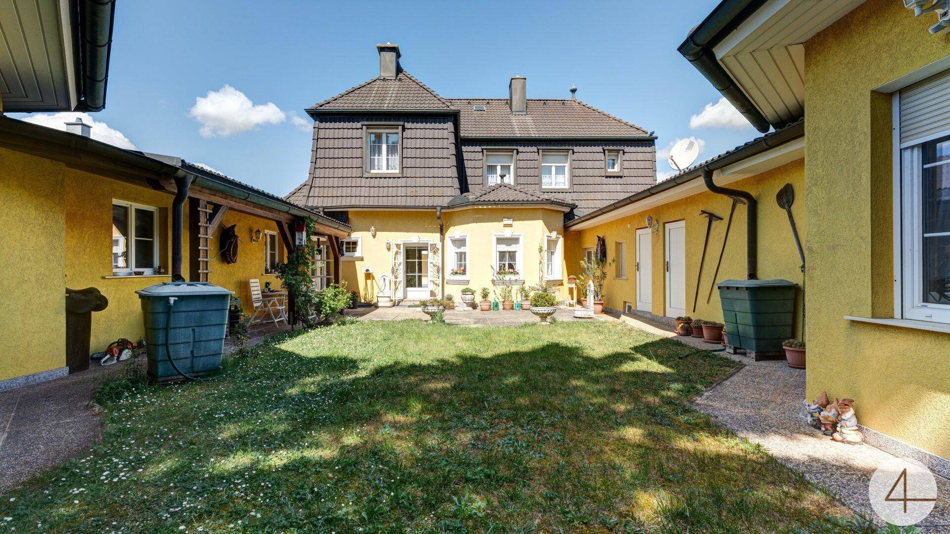 Sonniger Innenhof mit Rasenfläche, umgeben von den gelben Gebäudeteilen des Anwesens unter blauem Himmel.