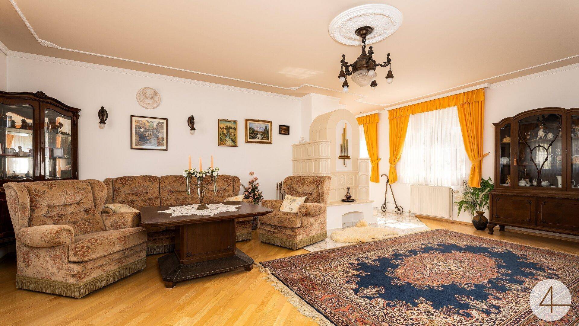 Gemütliches Wohnzimmer mit traditionellem Kachelofen, Parkettboden und einem orientalischen Teppich.