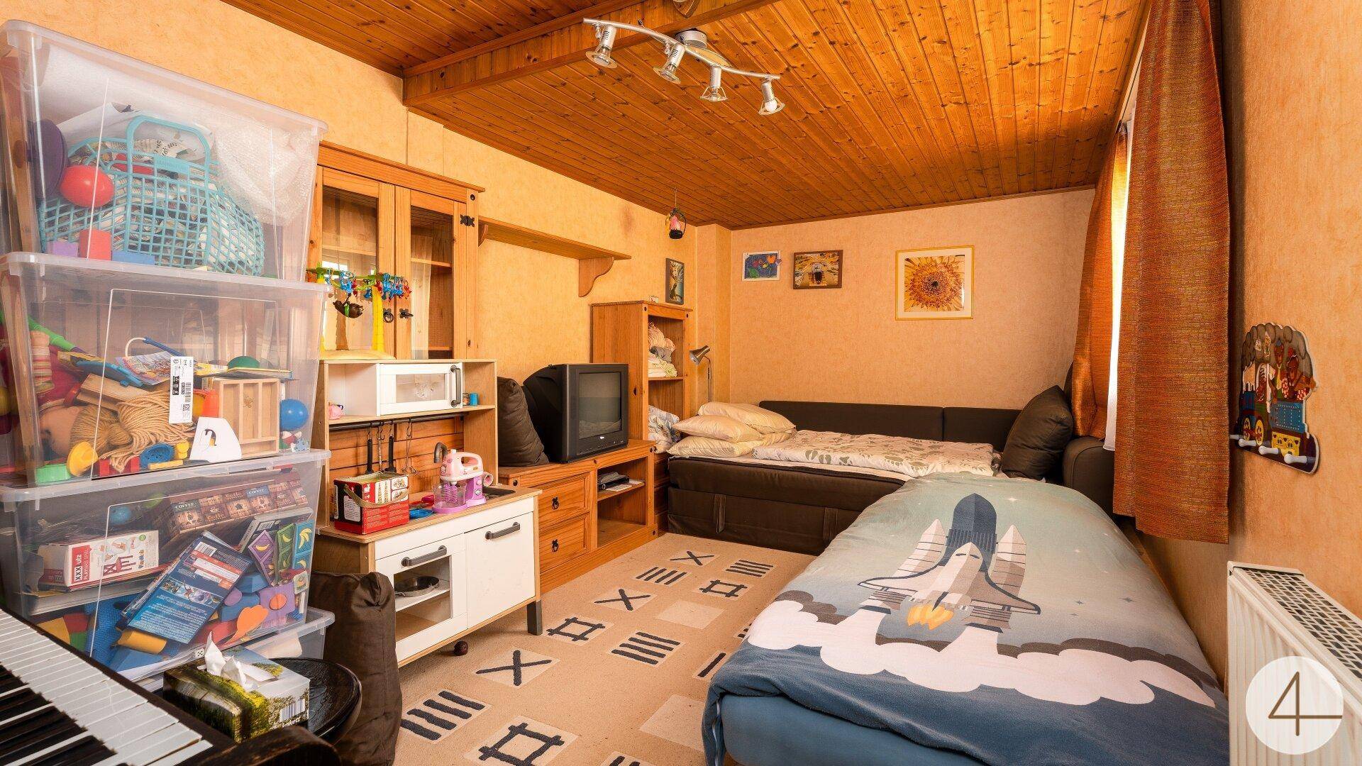 Gemütliches Schlafzimmer mit Holzbalkendecke, Spielzeug und einem Bett mit Weltraum-Motiv.
