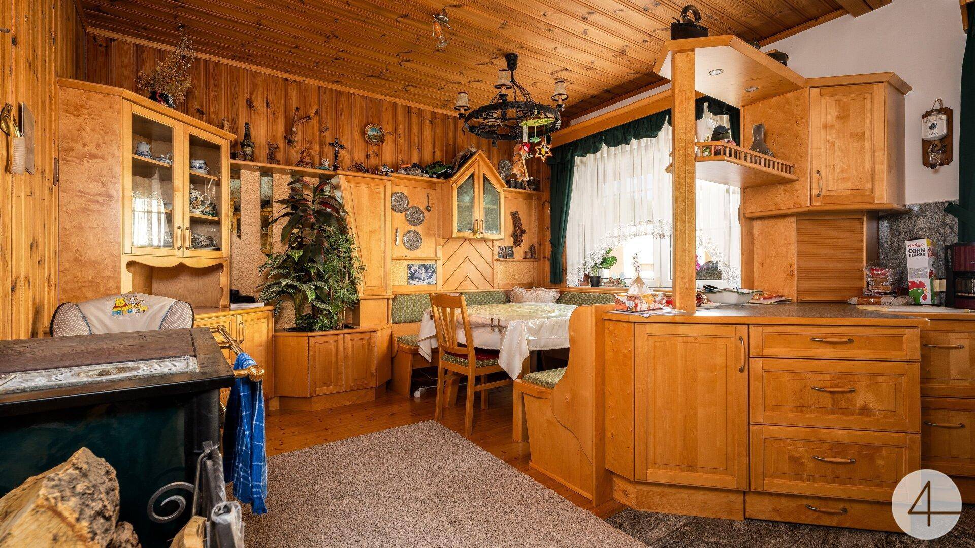 Traditionelle Holzküche mit Essecke, Einbauschränken und einem Kachelofen im alpenländischen Stil.