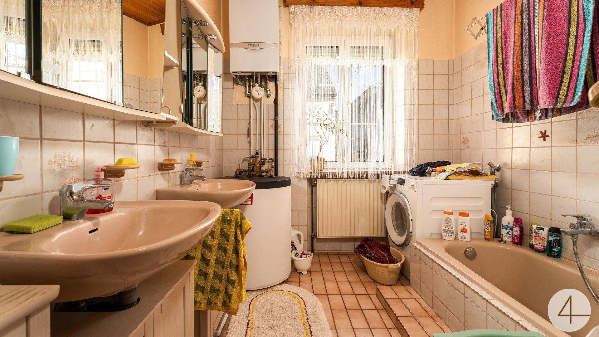 Funktionales Badezimmer mit zwei Waschbecken, Badewanne, Waschmaschine und einem Fenster.