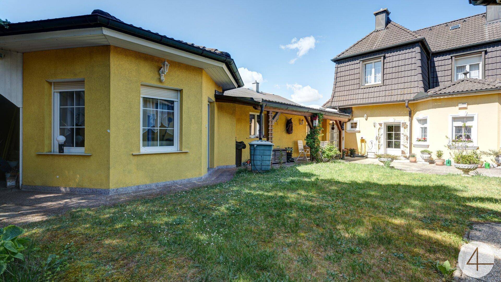 Sonniger Innenhof mit Rasenfläche, umgeben von den gelben Gebäudeteilen des Anwesens unter blauem Himmel.
