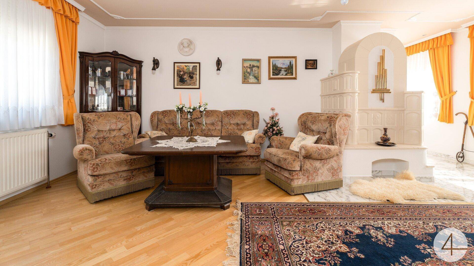 Gemütliches Wohnzimmer mit traditionellen Möbeln, einem großen Teppich und einem Kachelofen.