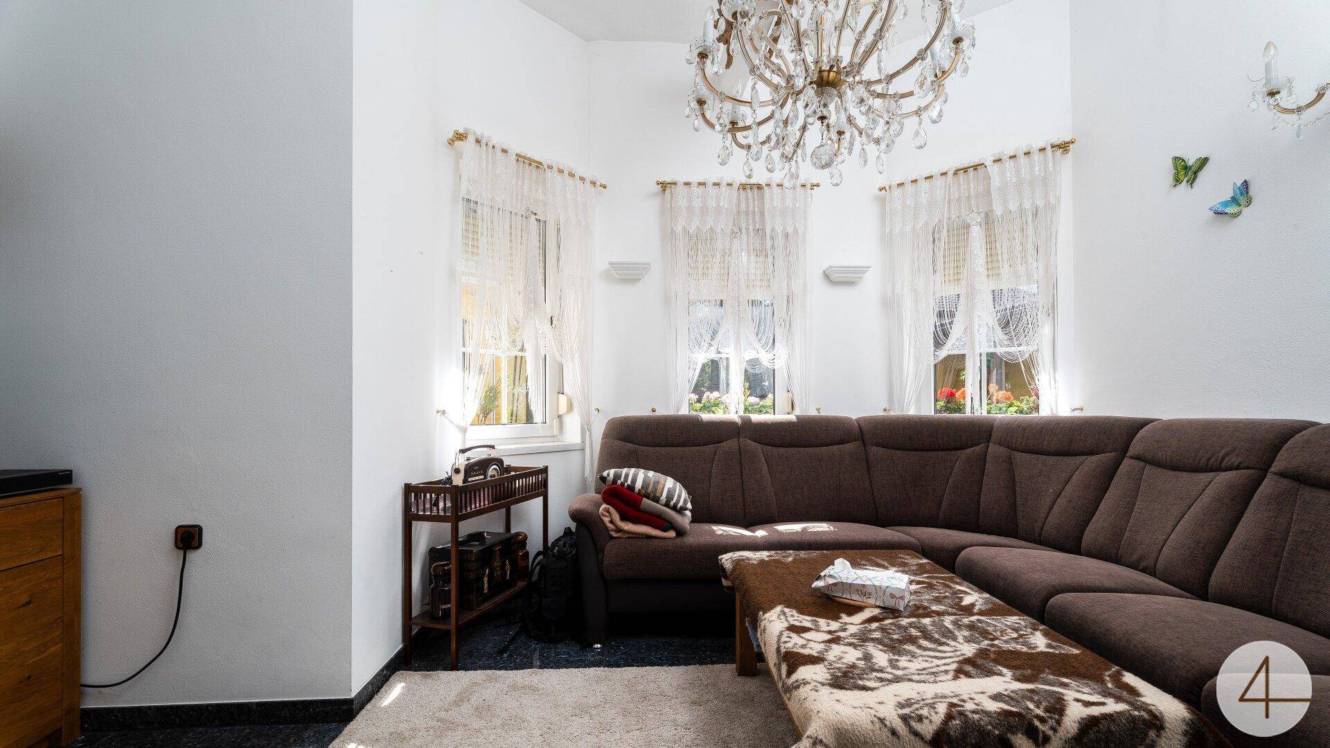 Helles Wohnzimmer mit großem Ecksofa, Kronleuchter und mehreren Fenstern für viel Tageslicht.