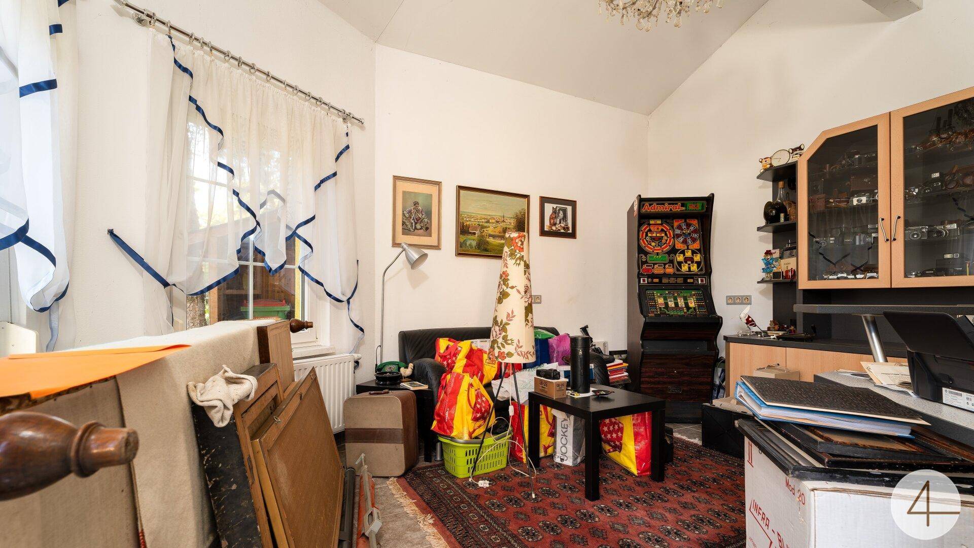 Vielseitiger Raum mit Schreibtisch, Spielautomat und verschiedenen persönlichen Gegenständen.