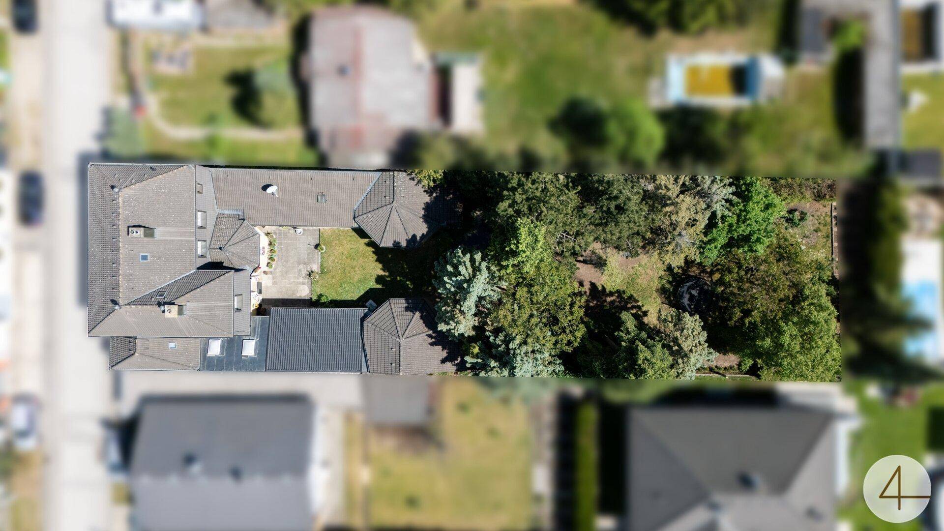Draufsicht auf das Anwesen mit seinen Gebäudestrukturen und dem angrenzenden bewaldeten Bereich.