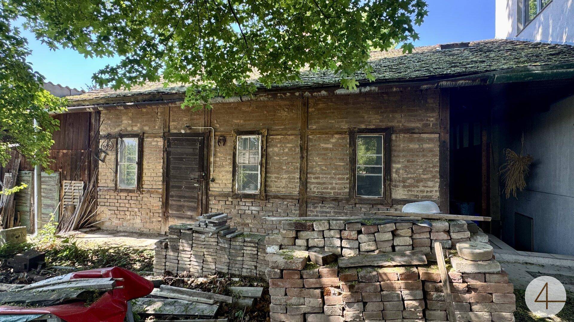 Rustikales altes Haus mit sichtbaren Ziegeln und Holzbalken, umgeben von Baumaterialien.