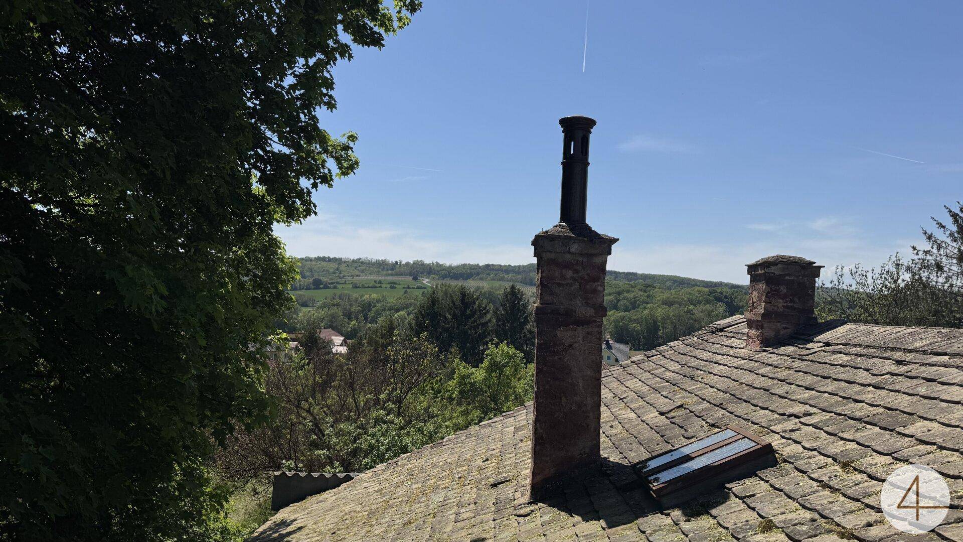 Dachansicht mit Schornstein und weitem Blick über eine grüne Hügellandschaft.