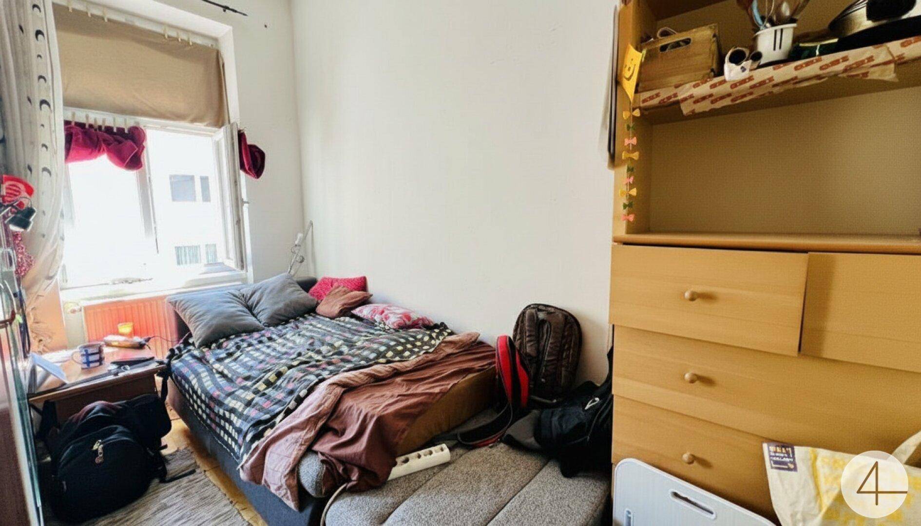 Gemütliches Schlafzimmer mit Einzelbett, Fenster und einem praktischen Holzregal für persönlichen Stauraum.