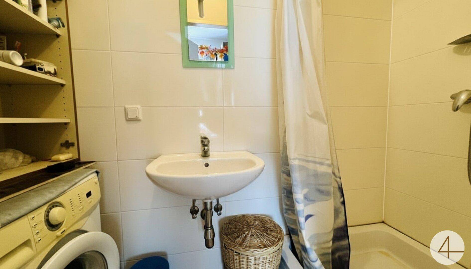 Funktionales Badezimmer mit weißen Fliesen, Waschbecken, Badewanne mit Duschvorhang und Waschmaschine.