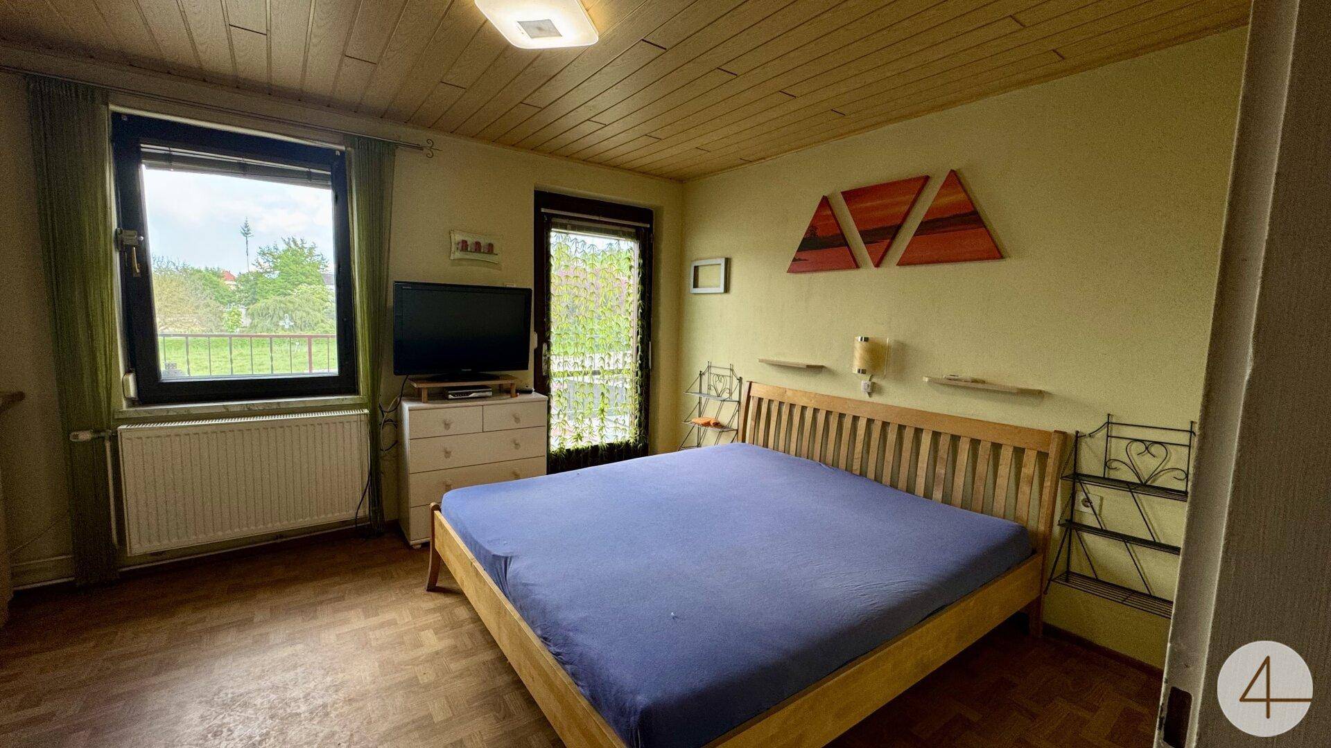 Schlafzimmer mit Holzbalkendecke, Parkettboden und Zugang zu einem kleinen Balkon.