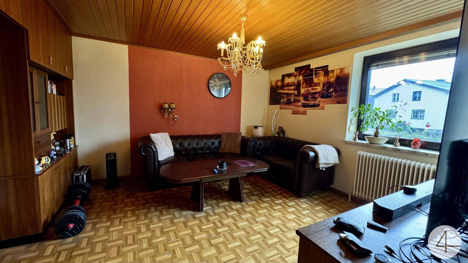 Wohnzimmer mit Holzbalkendecke, Parkettboden, Ledersofa und Kronleuchter.