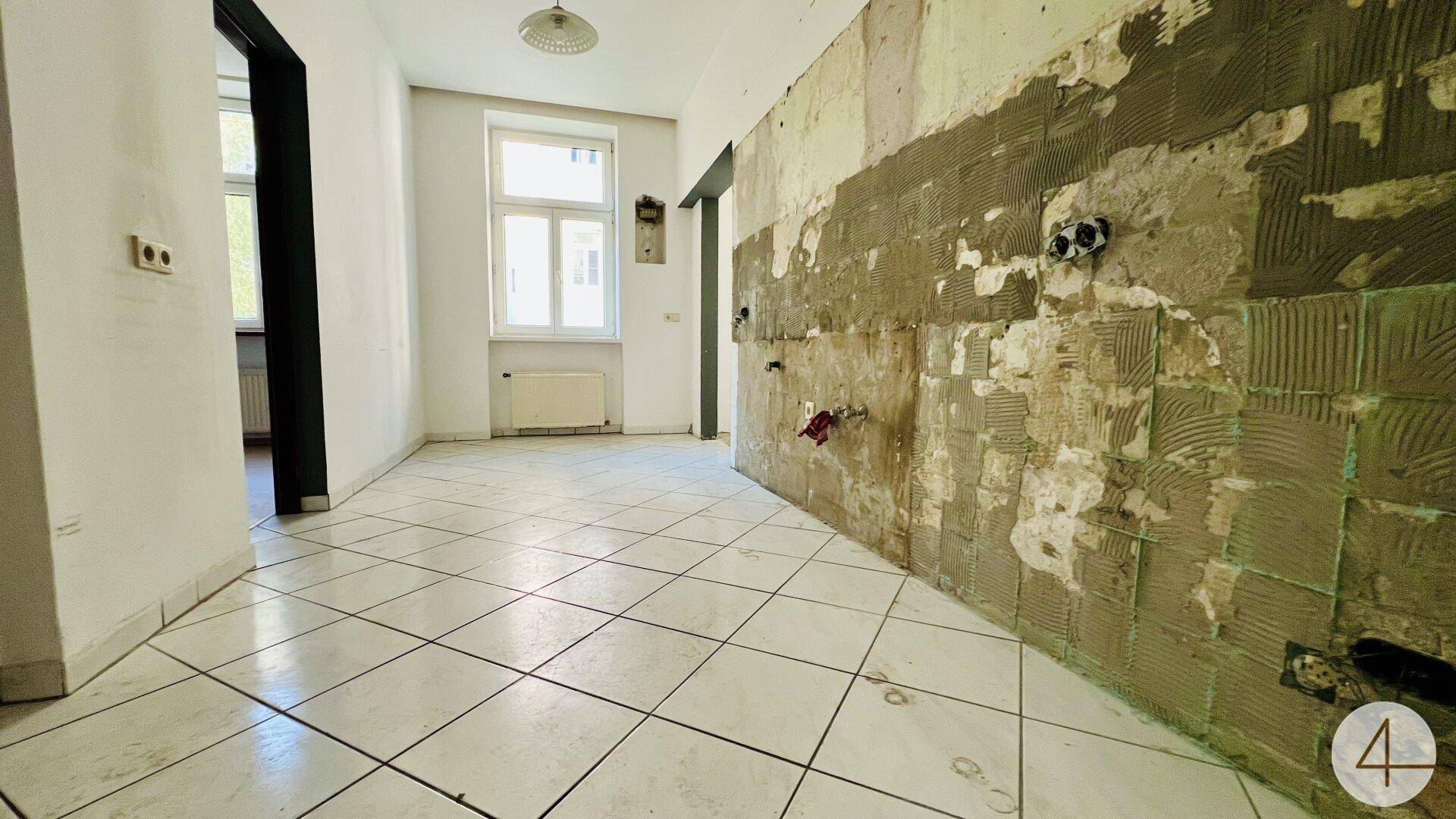 Renovierungsbedürftige Küche mit Fliesenboden und vorbereiteten Anschlüssen.