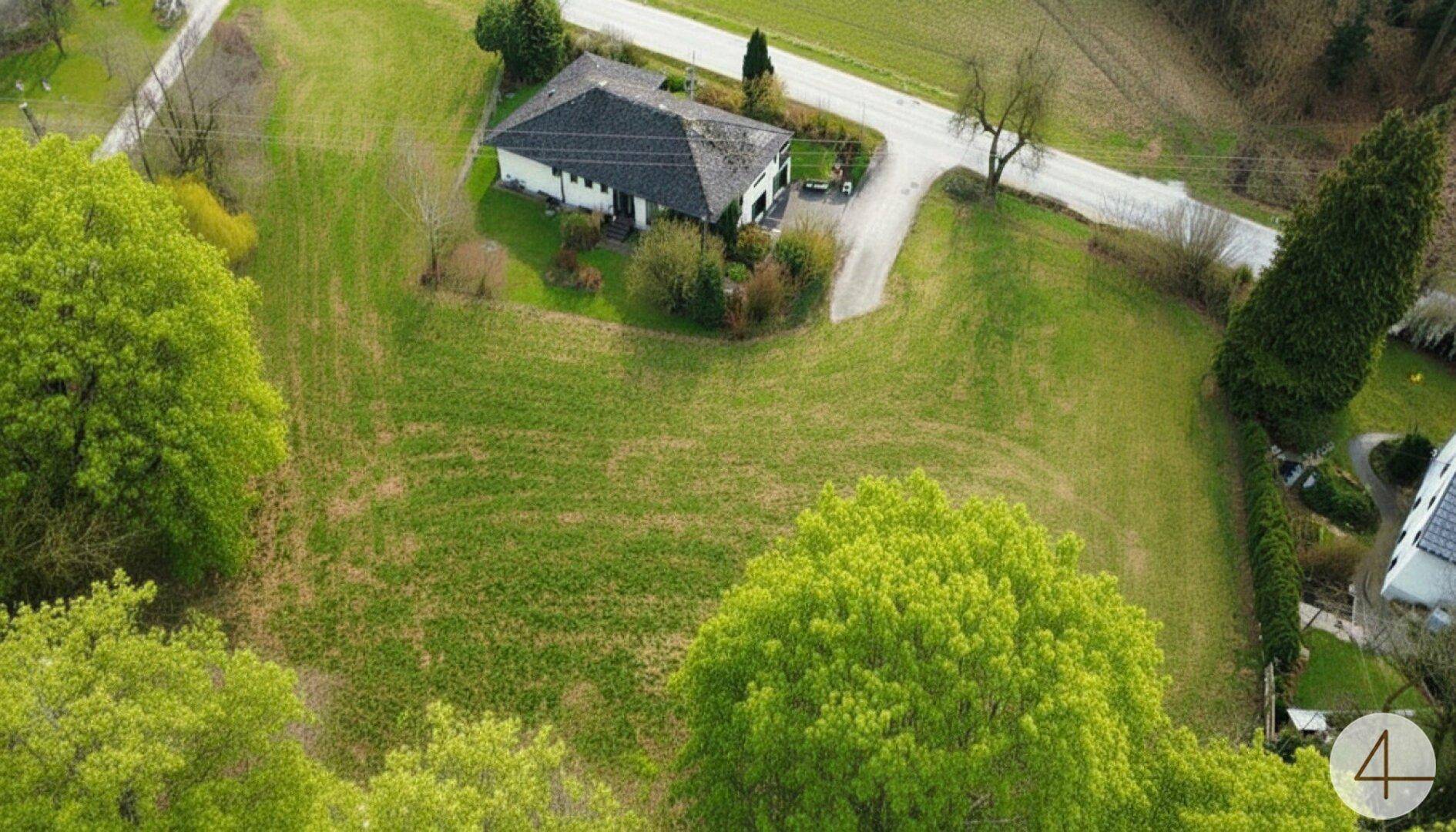 Luftaufnahme eines Hauses umgeben von weitläufigen grünen Feldern und Bäumen.