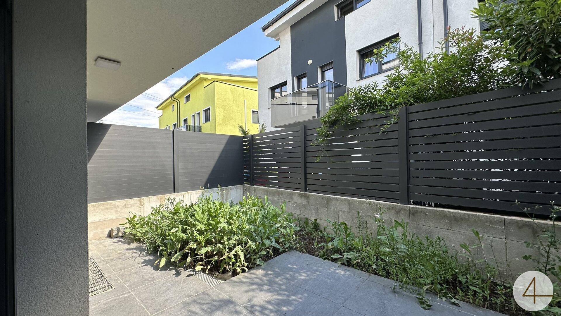 Kleiner Gartenbereich mit gepflasterter Terrasse und grünen Pflanzen, umgeben von einem Zaun.