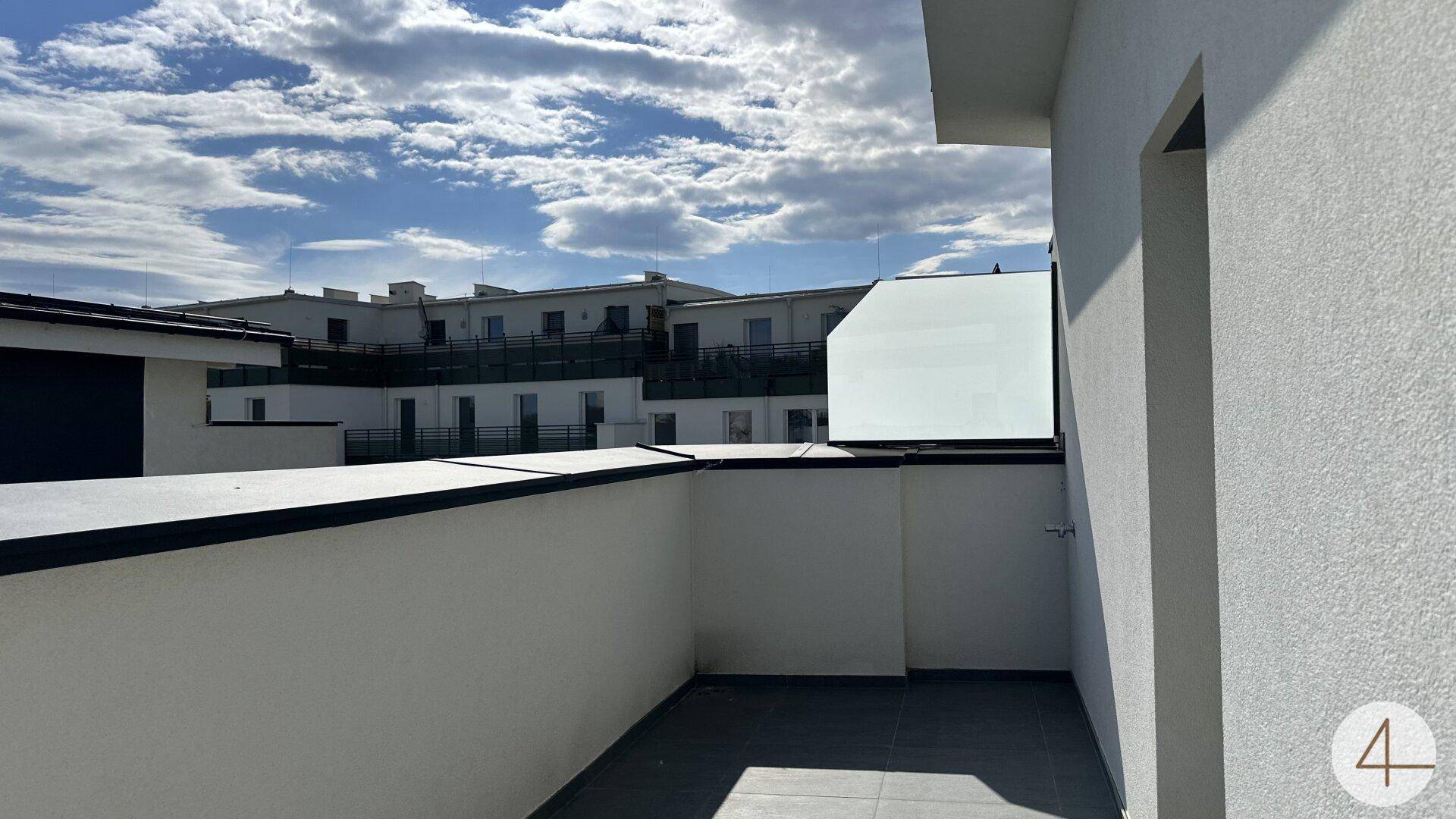 Leere Terrasse mit weißen Wänden und Blick auf die umliegenden Gebäude unter blauem Himmel.
