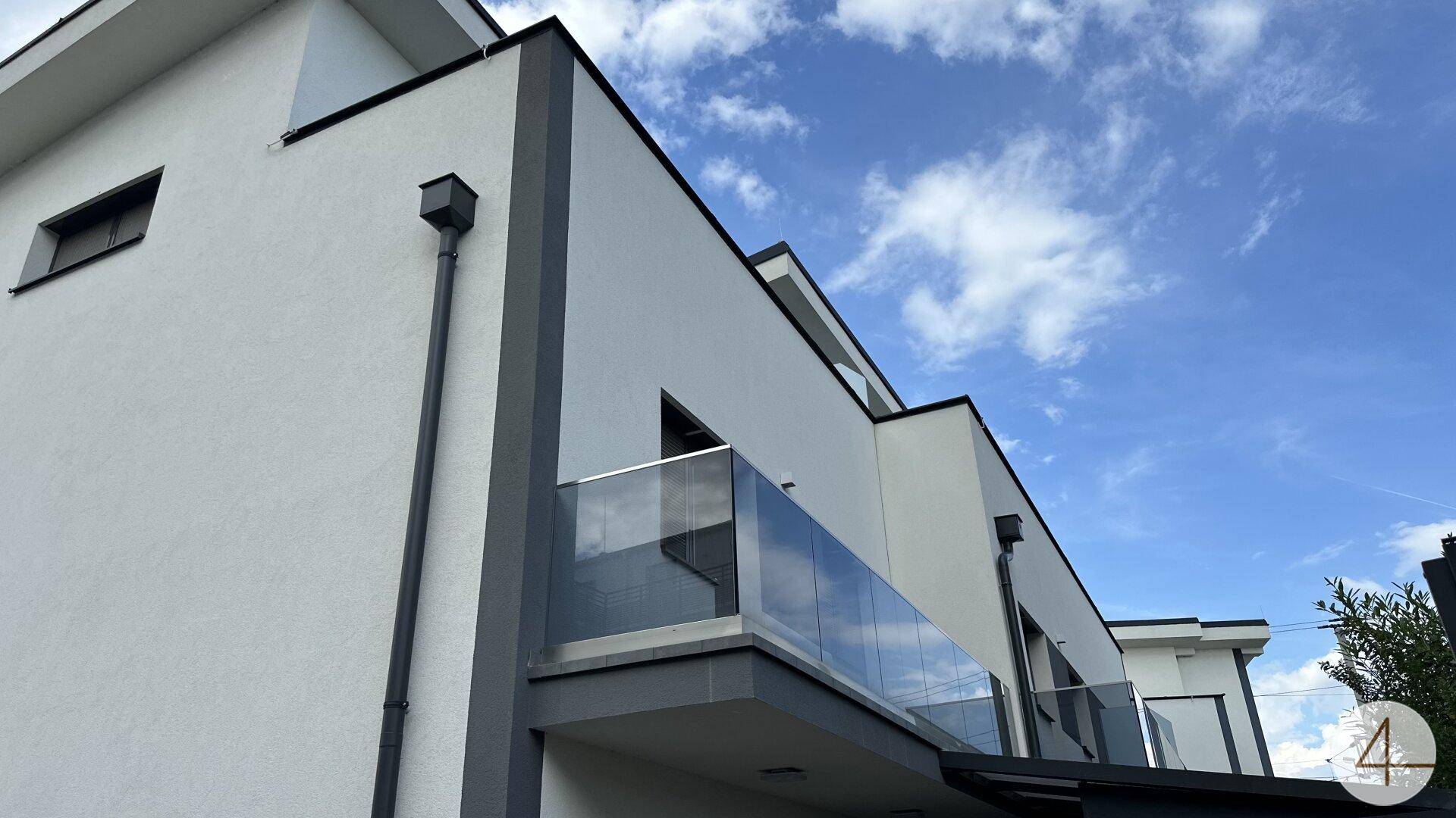Seitenansicht des modernen Gebäudes mit Balkonen und Glasgeländern unter blauem Himmel.