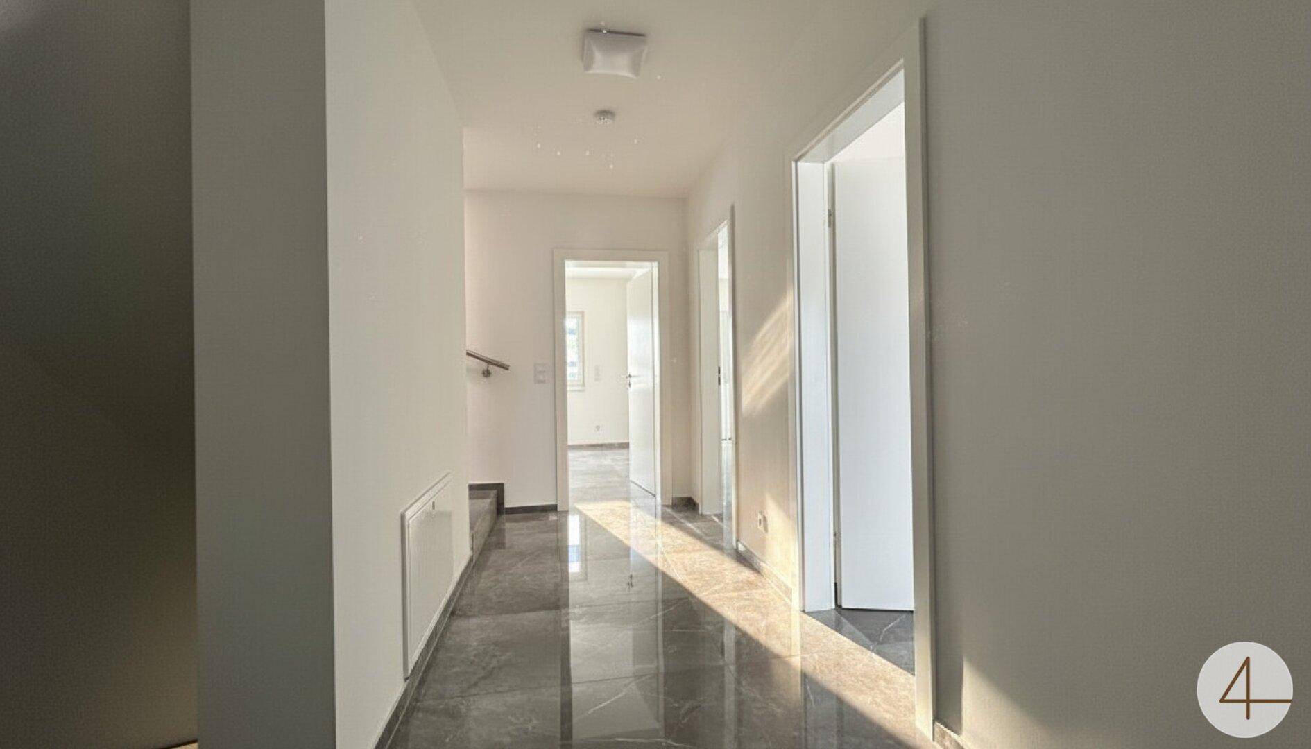 Heller Flur mit glänzenden Fliesenböden und viel natürlichem Licht durch die Fenster.