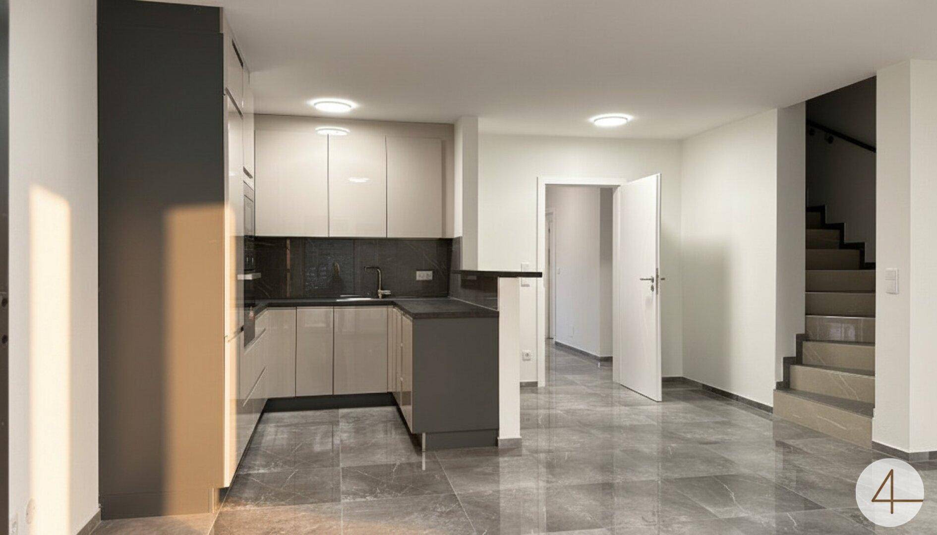 Moderne offene Küche mit hellen Schränken, dunklen Arbeitsplatten und glänzenden Fliesenböden.