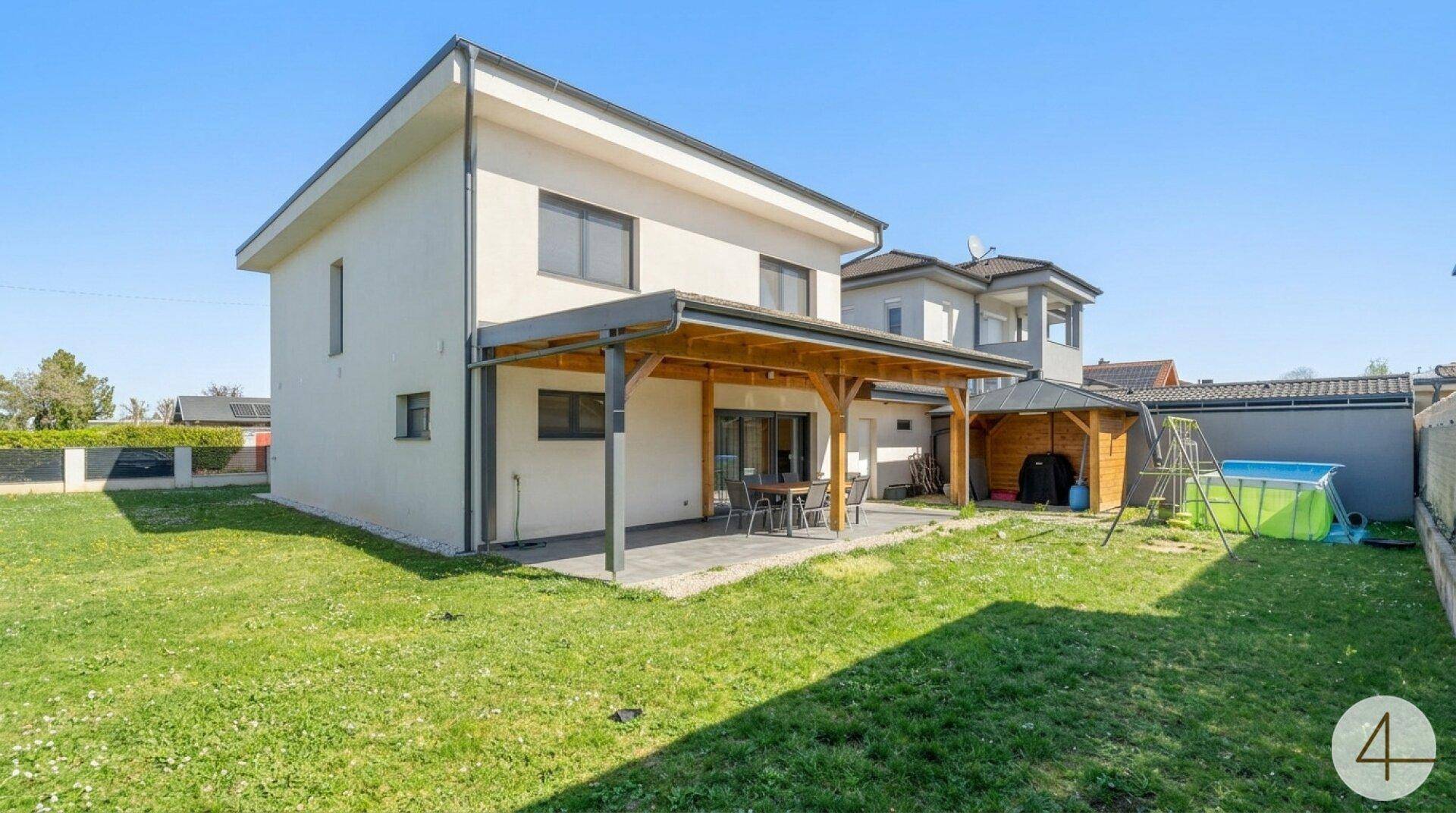 Geräumiger Gartenbereich mit überdachter Terrasse, Rasenfläche und kleinem Aufstellpool hinter dem modernen Haus.