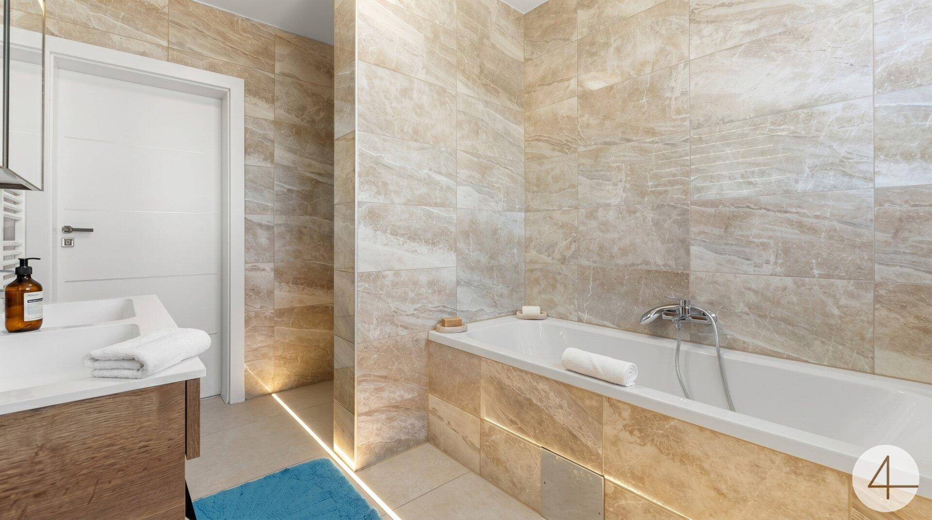 Elegantes Badezimmer mit Badewanne, beigefarbenen Fliesen und indirekter Beleuchtung.