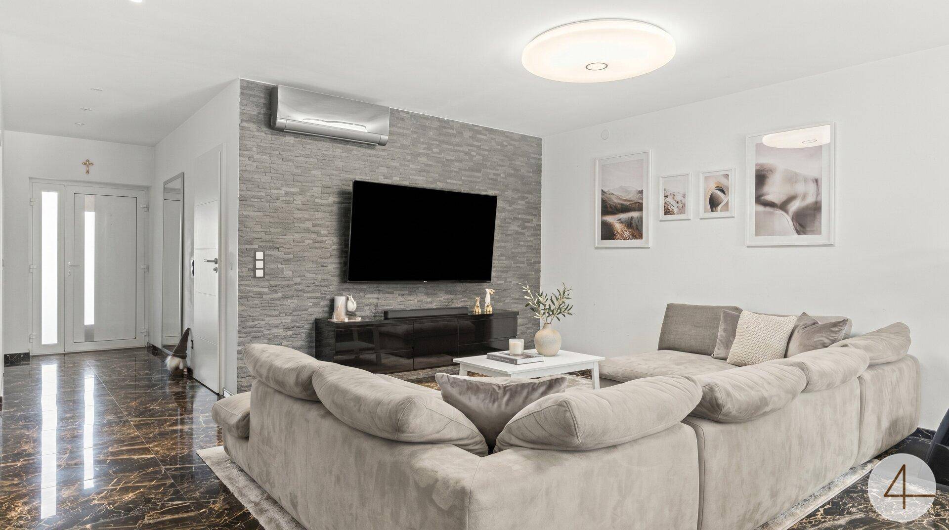 Gemütliches Wohnzimmer mit großem Ecksofa, Wandfernseher und dekorativer Steinwand.