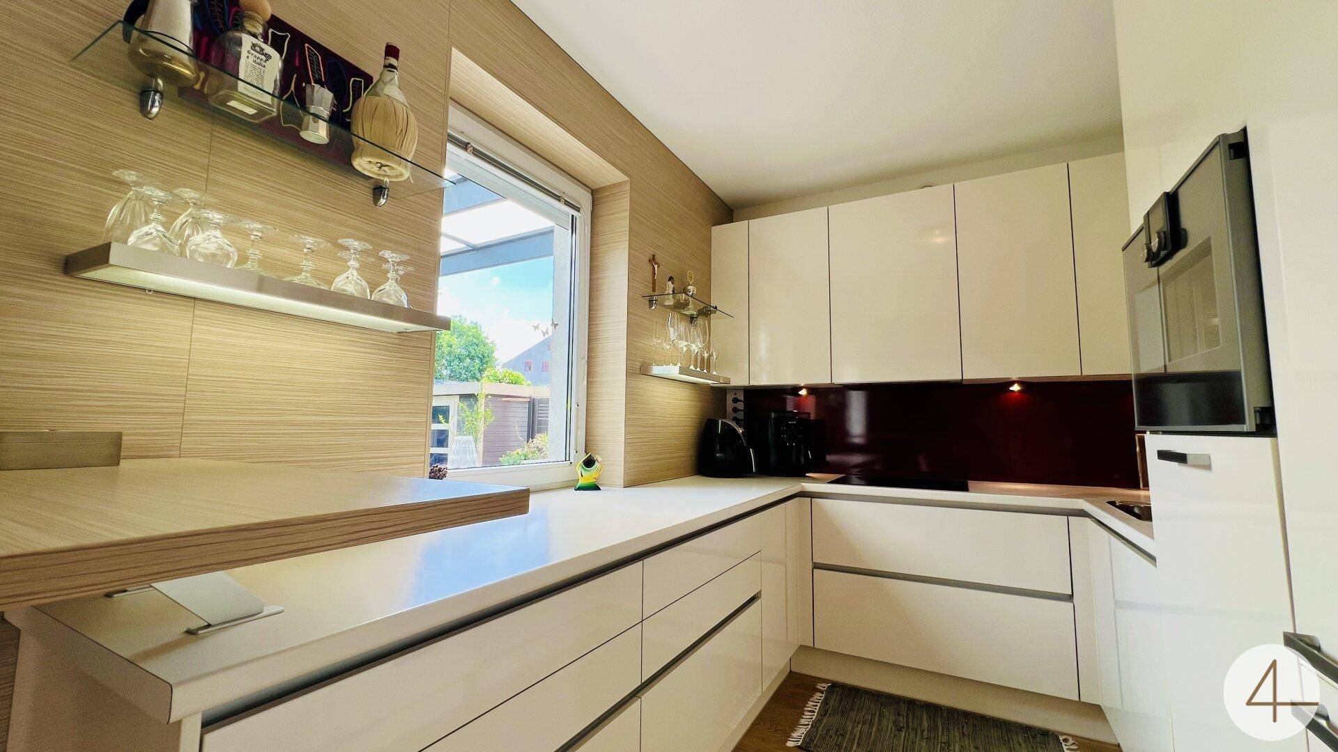Moderne Einbauküche mit weißen Hochglanzfronten, hellen Arbeitsplatten und Fenster.