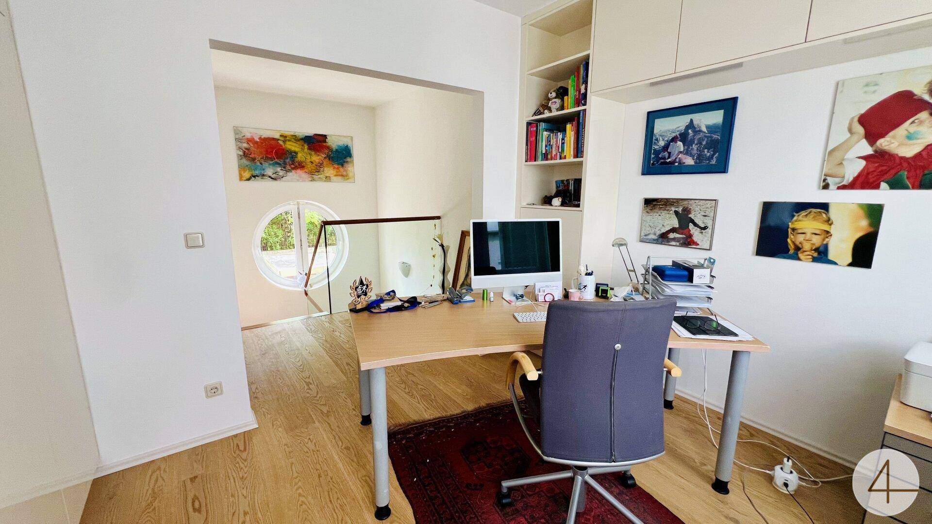 Helles Arbeitszimmer mit Schreibtisch, Regal und einem einzigartigen runden Fenster.