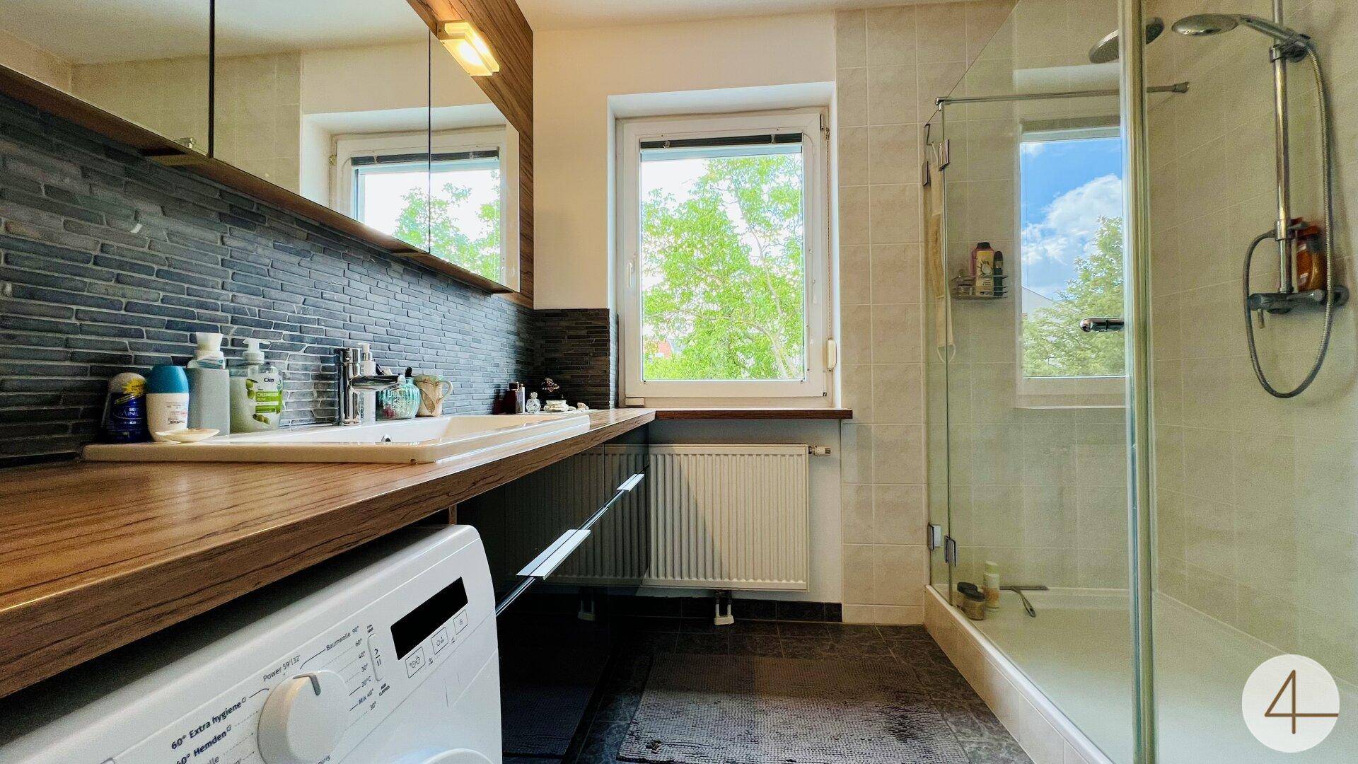 Modernes Badezimmer mit Dusche, Waschbecken und Fenster, inklusive Waschmaschine.