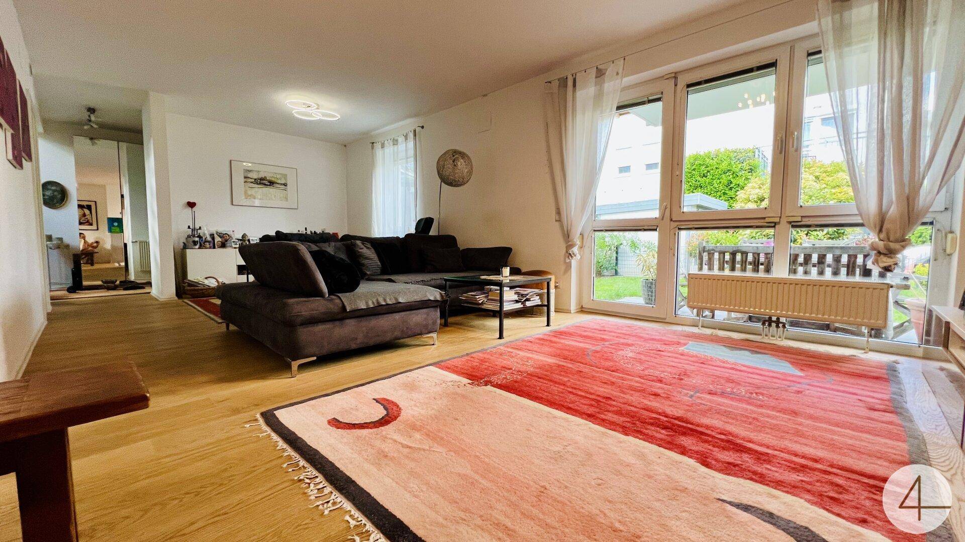 Helles Wohnzimmer mit Holzboden, großem Sofa und Zugang zu einem Außenbereich.