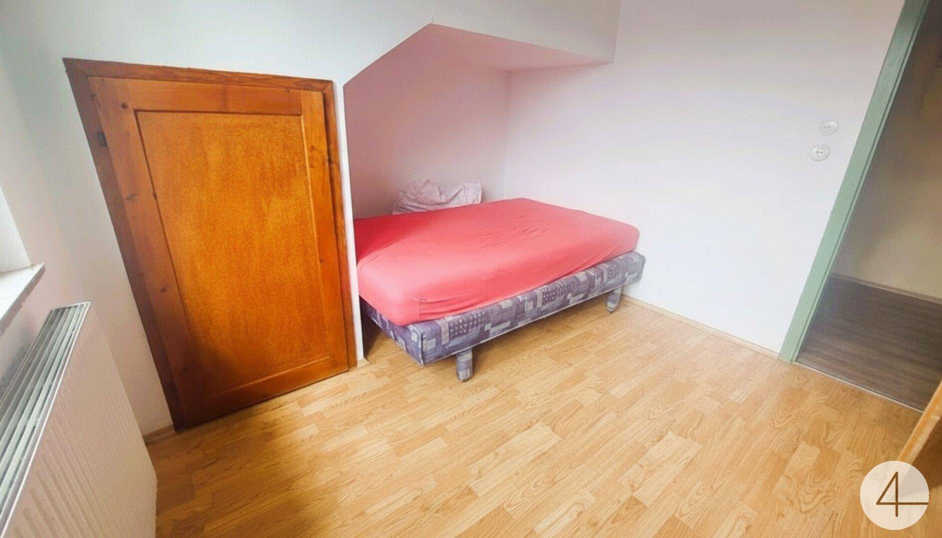 Kleines Schlafzimmer mit Holztür, Bett und Dachschräge, ausgestattet mit Laminatboden.