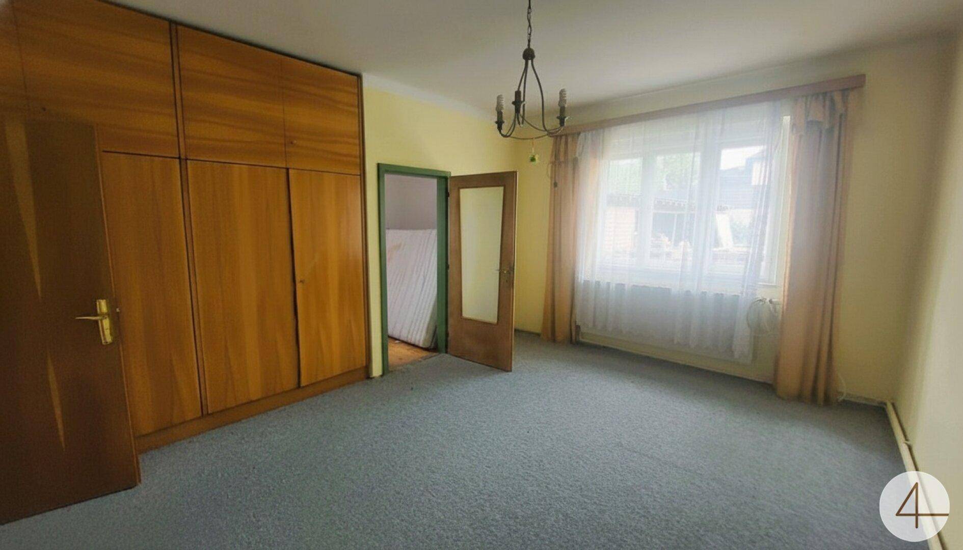 Geräumiges Schlafzimmer mit Teppichboden, großem Holzschrank und Fenster mit Vorhängen.