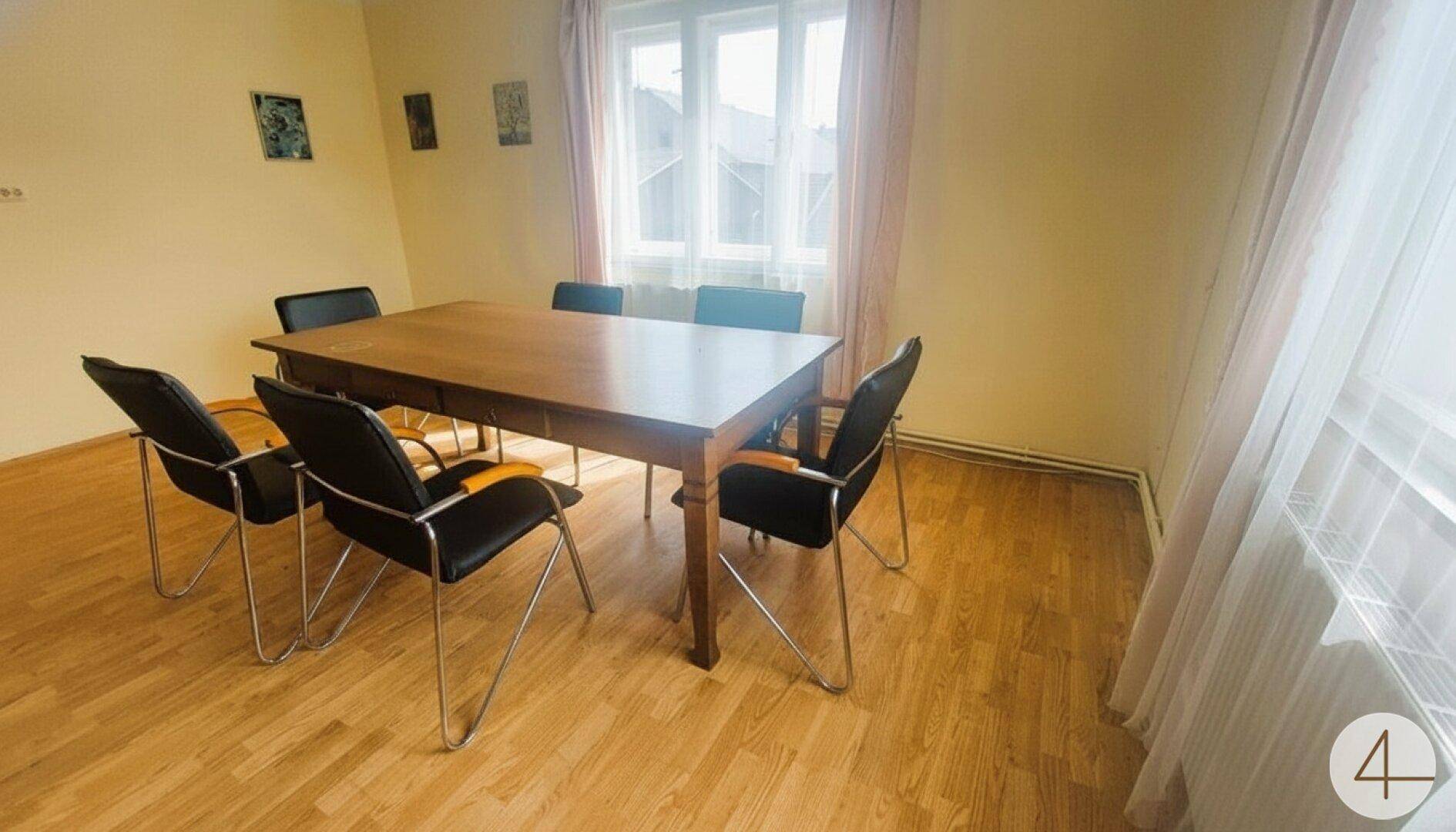 Essbereich mit Holztisch, schwarzen Stühlen und Laminatboden, hell durch großes Fenster.