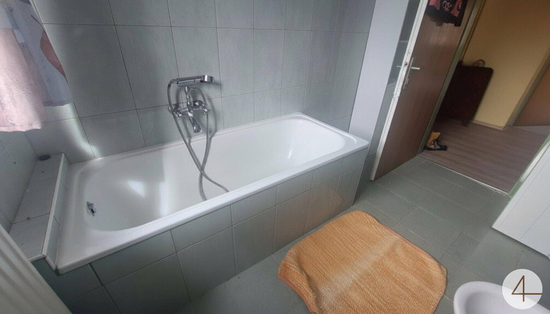 Badezimmer mit Badewanne und hellgrauen Wand- und Bodenfliesen, funktional gestaltet.