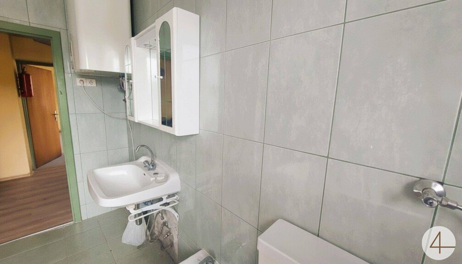 Kleines WC mit Waschbecken, Spiegelschrank und hellgrauen Fliesen an den Wänden.
