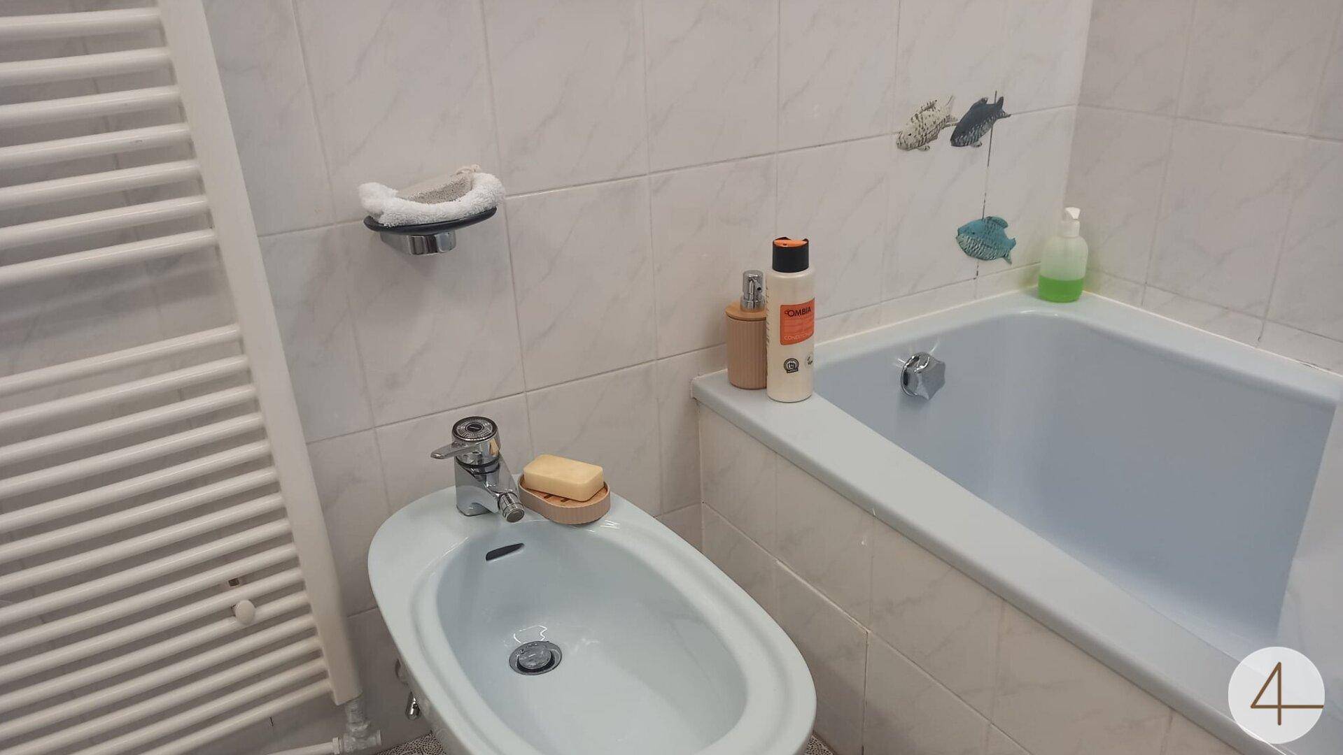 Badezimmer mit hellblauer Badewanne, Bidet und beheiztem Handtuchhalter, komplett gefliest.